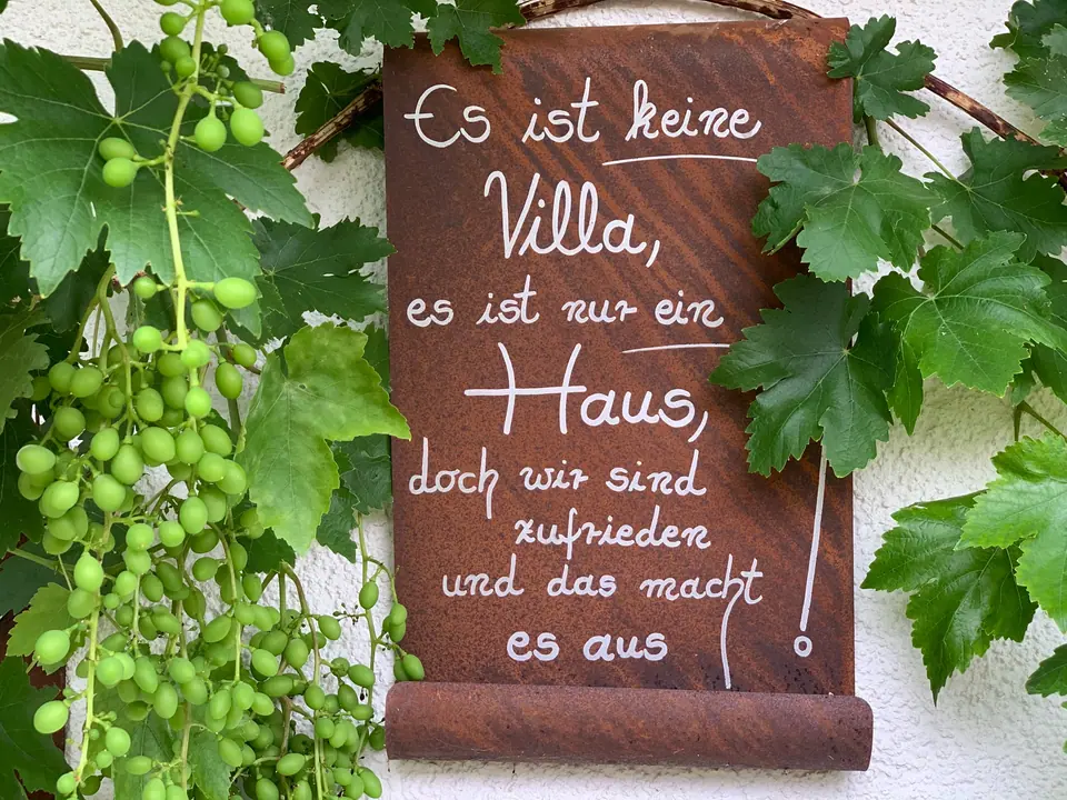 Kreidetafel zwischen Weinreben im Hof: Es ist keine Villa, es ist nur ein Haus, doch wir sind zufrieden und das macht es aus